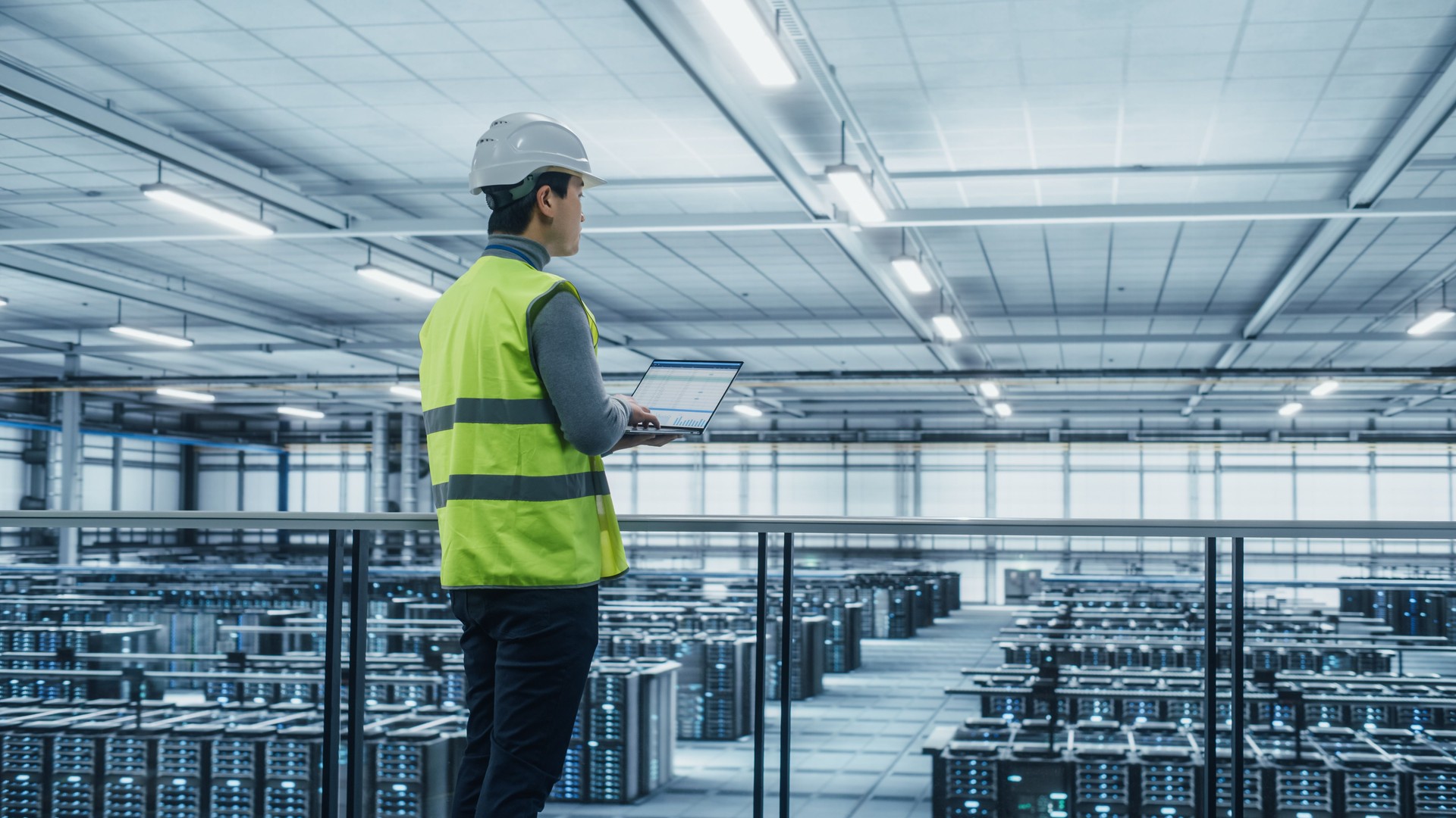 Data Center Engineer in High Visibility Vest Using Laptop Computer. Server Farm Cloud Computing Facility with Asian Male System Administrator Working with Data Protection Network for Cyber Security.